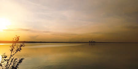The sun at sunset over a branch of a large lake and factories on the horizonの写真素材