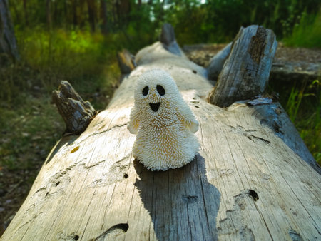 A small white ghost toy that smiles and stands on an old dry tree lit by the sun