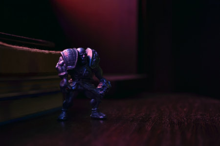 Kopeysk, Russia - August 10, 2021. A figurine of an evil bald warrior in armor with a skull stands on a wooden table next to books and is illuminated with purple light against a dark backgroundのeditorial素材