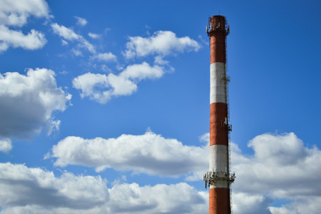 White and red boiler room chimney against the background of a beautiful blue sky and white clouds