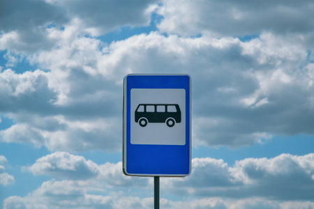 Blue and white bus stop sign depicting a bus against white clouds and a blue skyの写真素材