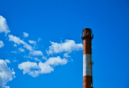 White and red boiler room chimney against the background of a beautiful blue sky and white cloudsの写真素材