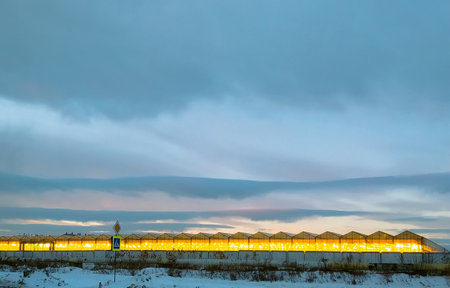 Greenhouses glowing yellow and a road sign against the backdrop of a winter landscape and the evening skyの写真素材