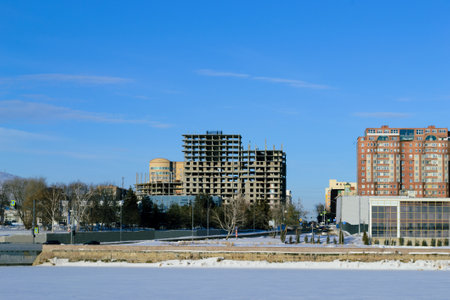 Unfinished building and completed buildings and frozen river against the blue sky