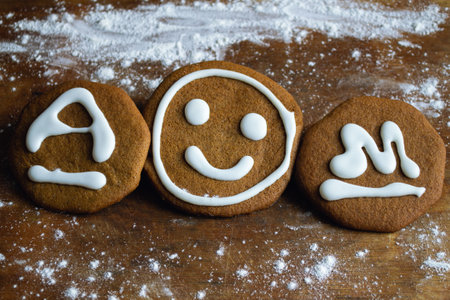 Three sweet cookies covered with white icing in the form of a smiley and the letters A and M lie on an old board surrounded by flourの写真素材