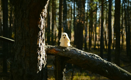 Sunlit ghost toy stands on a broken tree trunk in the forestの写真素材
