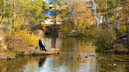 Chelyabinsk Russia - October 14, 2022. Gagarin Park. Father and daughter sit by the pond and look at the floating ducks in the autumn parkのeditorial素材