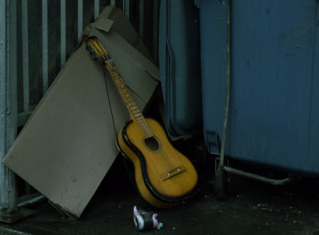 Discarded acoustic guitar stands near the trash canの写真素材