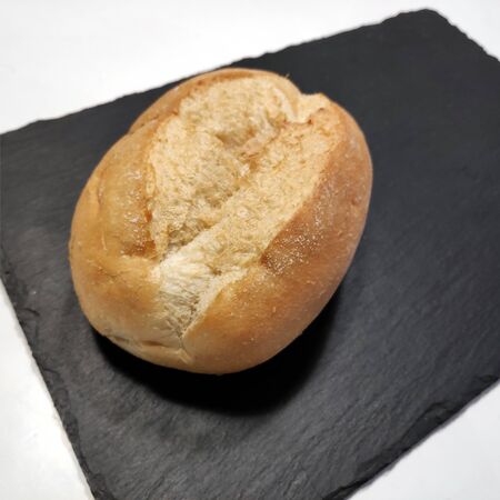 Fresh bread, crispy wheat roll on a black stone base. Kaiser roll.
