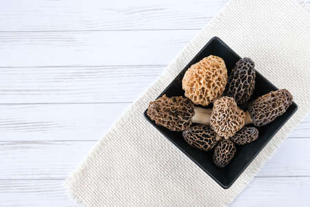 A few spring morel mushrooms lie in a black square plate, on a cloth, on a table. the concept of...
