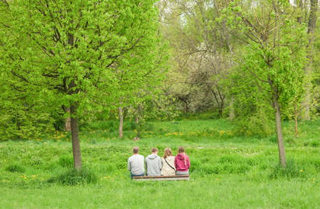 Four people sit on a bench in the park. The family rests in the spring in nature. High quality photoの写真素材