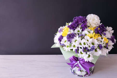 Bouquet of white, purple and yellow flowers in a box with a white-purple bow. Floral arrangement on a black background. A postcard to congratulate you on your birthday, the beginning of the school year or other holidays. Space for your text. High quality photoの写真素材