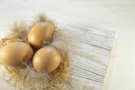 Three orange eggs lie in a nest on a table, on wooden boards. Easter card for the holiday. High...