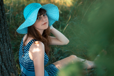 Young happy girl sitting under a tree on a summerの写真素材