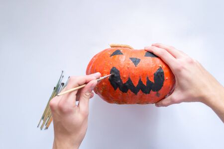 Male hands decorate a Halloween pumpkin on a white backgroundの写真素材