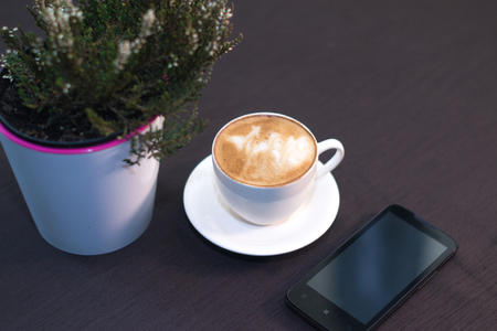 A cup of coffee, a smartphone in a cafe with a blurred backgroundの写真素材
