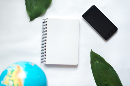 Notepad on white background with globe, green leaf of tropical plantの写真素材
