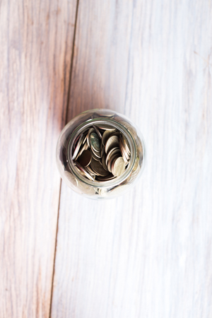 Glass jar with coins on a wooden background.の写真素材