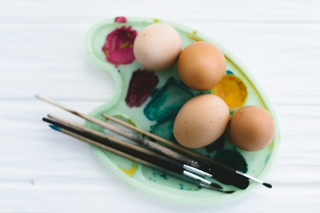 The process of painting Easter eggs still life on a white wooden background.の写真素材