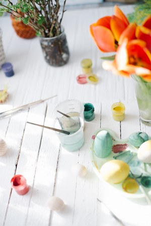 The process of painting Easter eggs still life on a white wooden background.の写真素材