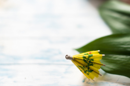 Yellow cocktail umbrella on sand on a wooden background.の写真素材