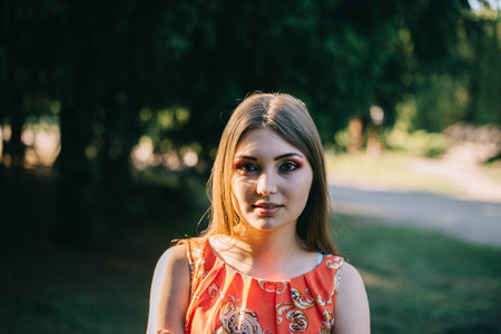 Beautiful young girl in a summer red dress in a park.の写真素材