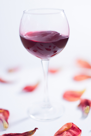 Red wine on a white background with rose petals.の写真素材