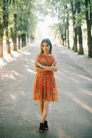 Beautiful young girl in a summer red dress in a park.の写真素材