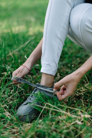 Girl athlete in a black T-shirt and white pants tying shoelaces on sneakers.の写真素材