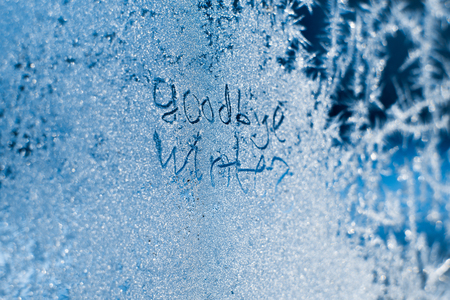 The inscription: goodbye, winter. On a frozen winter window in frosty patterns.の写真素材