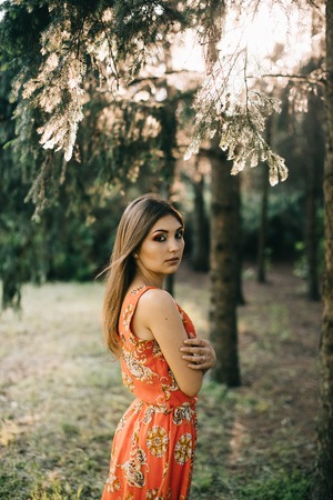 Beautiful young girl in a summer red dress in a park.の写真素材