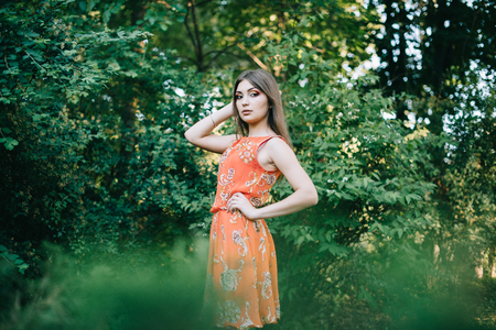 Beautiful young girl in a summer red dress in a park.の写真素材