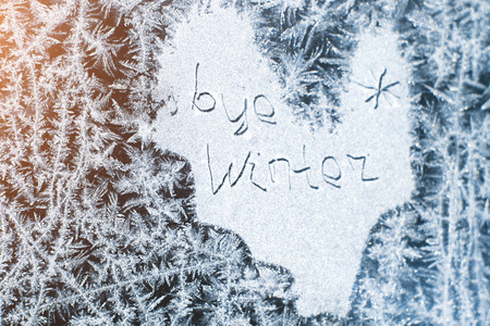 The inscription: goodbye, winter. On a frozen winter window in frosty patterns.の写真素材