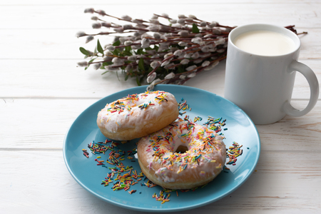Donuts on a blue plate with a cup of milk on a white wooden background.の写真素材