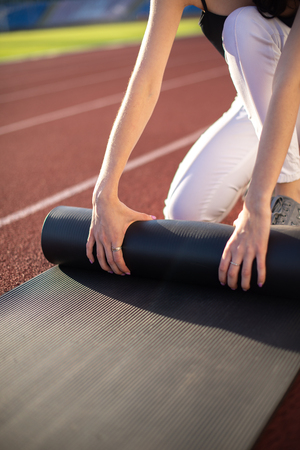 Athlete girl twists her mat after playing sports on a sunny summer day at the stadium.の写真素材