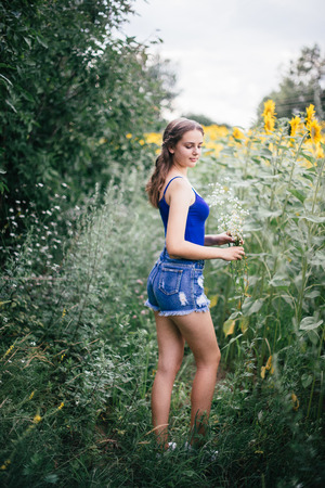 A girl in short shorts and a blue T-shirt with a bouquet of wild flowers.の写真素材