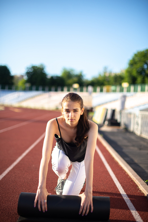 Athlete girl twists her mat after playing sports on a sunny summer day at the stadium.の写真素材