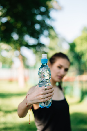 Girl athlete with a bottle of water in her hands. Summer sunny day in the park.の写真素材