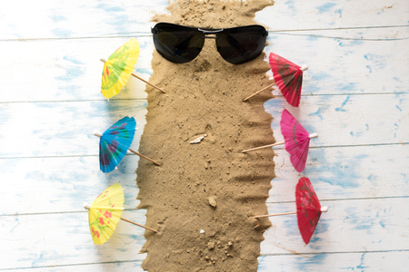 Beach still life. Black glasses with cocktail umbrellas, seashell on sand on a wooden background.の写真素材