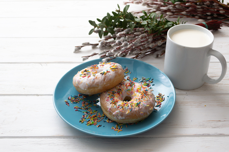 Donuts on a blue plate with a cup of milk on a white wooden background.の写真素材