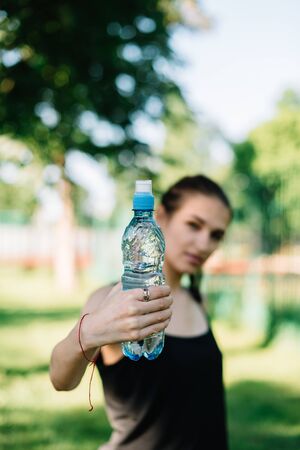 Girl athlete with a bottle of water in her hands. Summer sunny day in the park.の写真素材