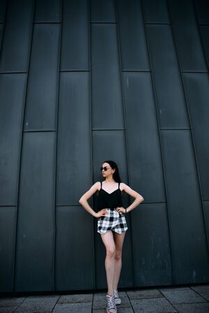 Sexy girl near a dark wall in a T-shirt, sunglasses and short shorts.の写真素材