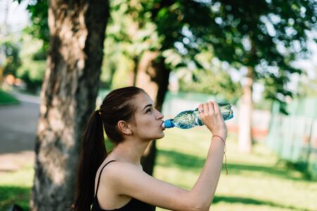Athlete girl drinks water after a workout in the park.の写真素材