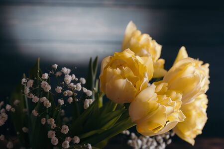 Yellow tulips in a vase on a wooden background.