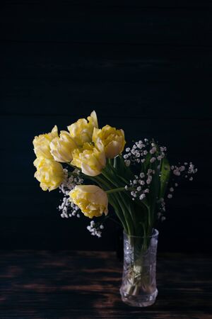 Yellow tulips in a vase on a wooden background.の写真素材