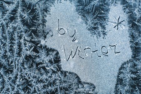 The inscription: goodbye, winter. On a frozen winter window in frosty patterns.の写真素材