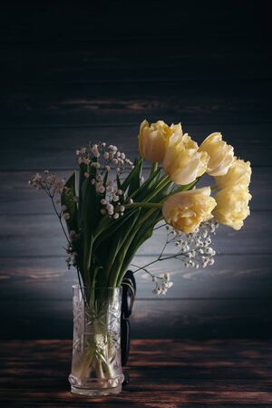 Yellow tulips in a vase on a wooden background.の写真素材