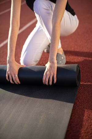 Athlete girl twists her mat after playing sports on a sunny summer day at the stadium.の写真素材