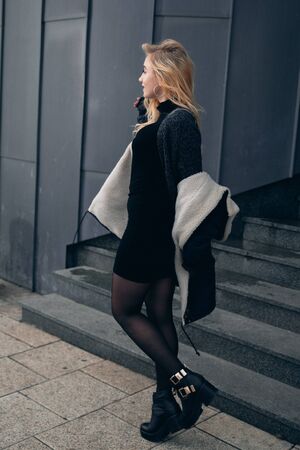 Girl in a black dress in the winter on a background of a dark building.の写真素材