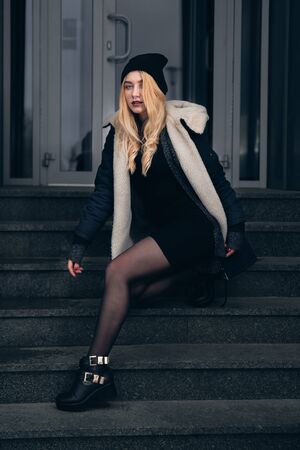 Girl in a black dress in the winter on a background of a dark building.の写真素材